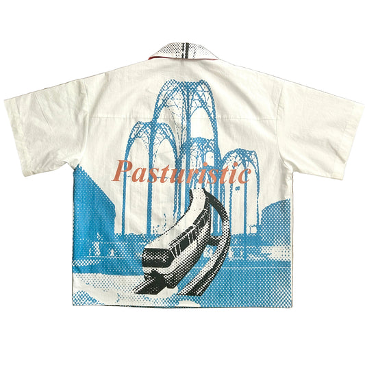 A white short-sleeve camp collar shirt laid flat, featuring a blue halftone graphic of a Monorail and Pacific Science Center arches, with the word 'Pasturinic' printed across the front in coral.