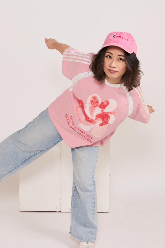 Person wearing a pink graphic sweatshirt, jeans, and cap on a white background