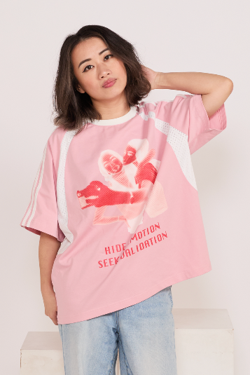 Person wearing a pink graphic t-shirt with text and graphics on a plain background