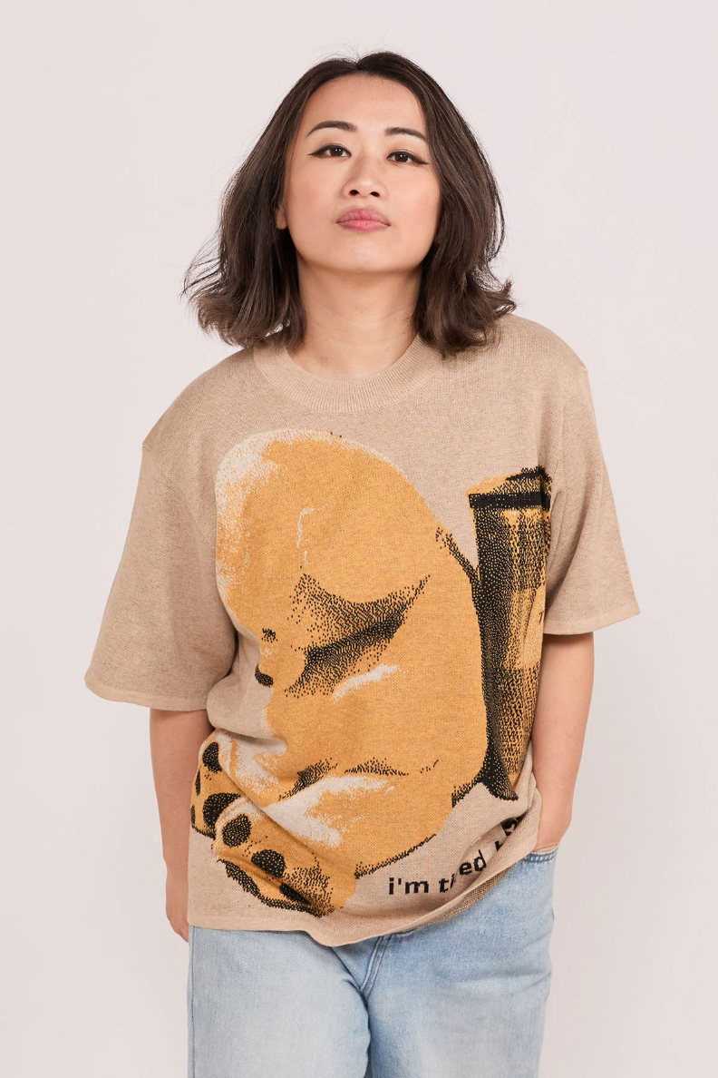 Person wearing a beige knitted shirt with a tired looking bear graphic design and texts saying "I'm tired, boss."