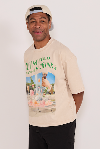 Man wearing a beige graphic t-shirt, black pants on a white background