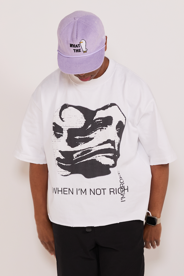 Person wearing a white t-shirt with a graphic design and text, paired with a purple cap on a plain background